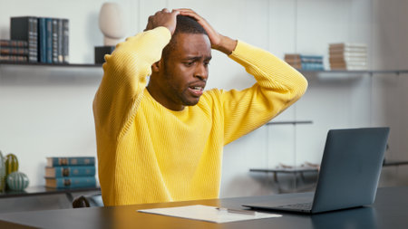 Upset man looks at laptop with lost internet connection holding hands on head sitting at the desk in the officeの写真素材