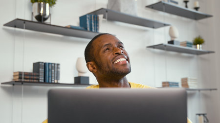Smiling young man working with laptop at the desk at homeの写真素材