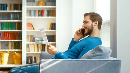 Young male talking on the phone in his home office against the background of bookshelvesの写真素材