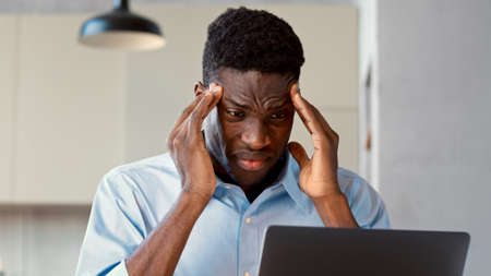 Emotional young man with headache working with laptop in officeの写真素材