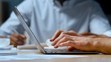 Office concept: young businessman typing on a computer keyboard against the backdrop of office work, close-upの写真素材