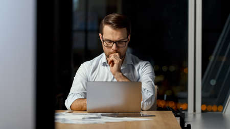 Young professional in a white shirt with a computer at work in the evening officeの写真素材