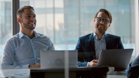 Applauding colleagues for corporate leader in meeting room. Two business partners communicating at...