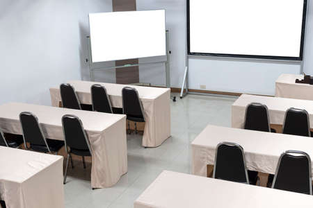Cream colored fabric table covers and brown armchairs with white board and white screen in the seminar room.の写真素材