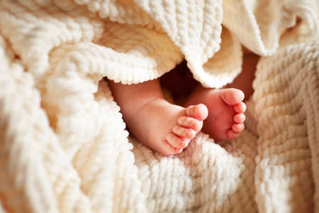 Cute feet of newborn baby on white plaid