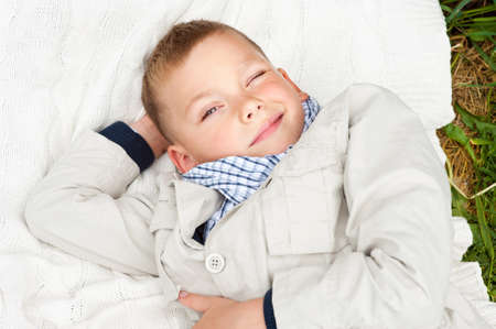 Smiling cute boy lying on white plaid on green grass and having funの写真素材