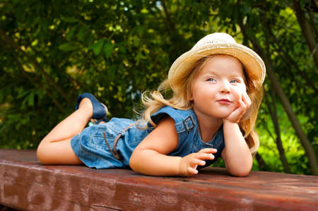 Funny toddler girl lying on bench in park and dreamingの写真素材
