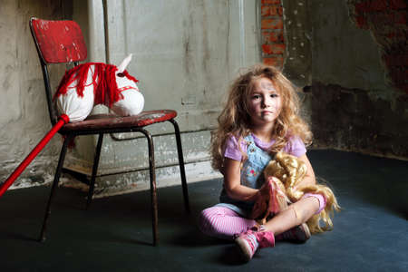 Dirty blond girl with dolls in basement sitting on floorの写真素材