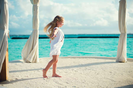 Adorable european toddler girl with long hair stays against wind on seasideの写真素材