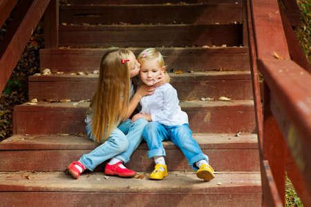 Two adorable european sisters holding each other and sitting on stairs in autumn parkの写真素材