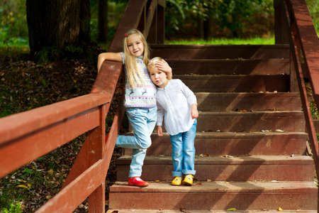 Two adorable european sisters holding each other and standing on stairs in autumn parkの写真素材