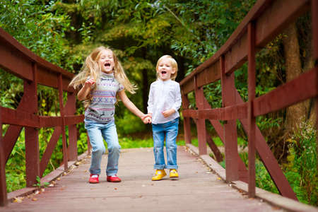 Two cute european blond sisters on scenic bridge together having fun with colorful summer forest on backgroundの写真素材