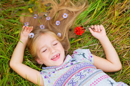 Happy toddler girl lies on grass in summer field with flowers in hair and smilingの写真素材
