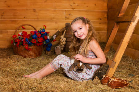 Beautiful happy girl with long blond hair playing with funny easter rabbit in hay in country houseの写真素材