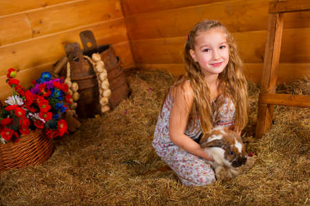 Beautiful happy girl with long blond hair playing with funny easter rabbit in hay in country houseの写真素材