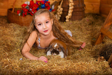 Beautiful happy girl with long blond hair playing with funny easter rabbit in hay in country houseの写真素材