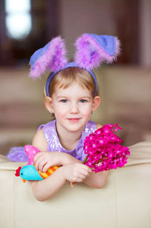 Happy funny little girl with colorful pink flowers and fancy bunny ears on head celebrates easter ...