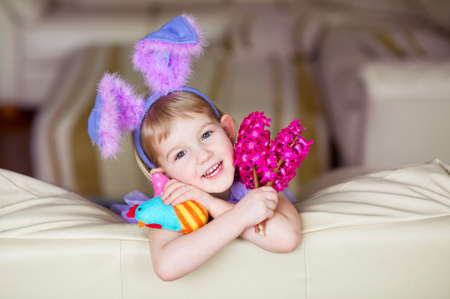 Happy funny little girl with colorful pink flowers and fancy bunny ears on head celebrates easter  Toy han in hands の写真素材