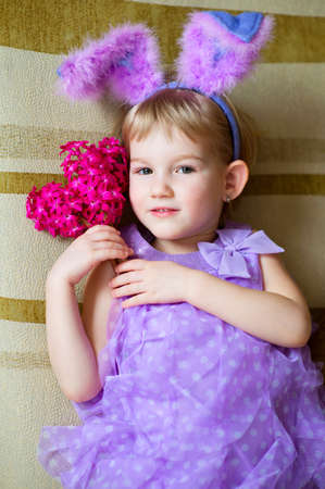 Happy funny little girl with colorful pink flowers and fancy bunny ears on head celebrates easter ...