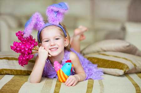 Happy funny little girl with colorful pink flowers and fancy bunny ears on head celebrates easter  Toy han in hands の写真素材