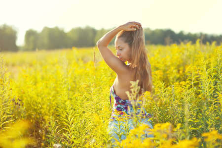 Happy european young woman in summer blooming field shaking her long hair and walking under evening sunの写真素材