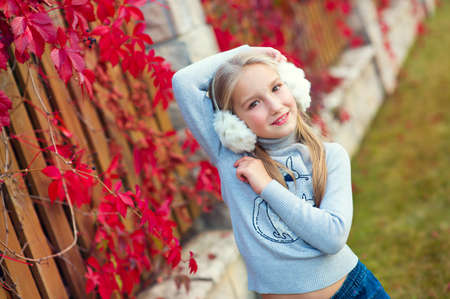 Very beautiful toddler blond girl posing in autuautumn garden with red plant