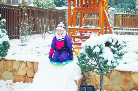 Happy emotional russian girl riding on slade in winter park with playground full of snowの写真素材