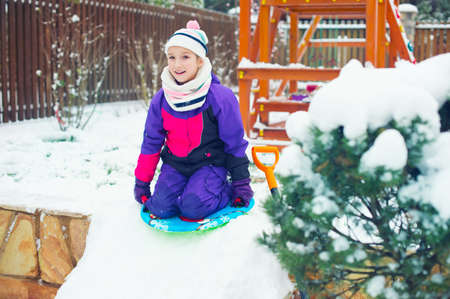 Happy emotional russian girl riding on slade in winter park with playground full of snowの写真素材