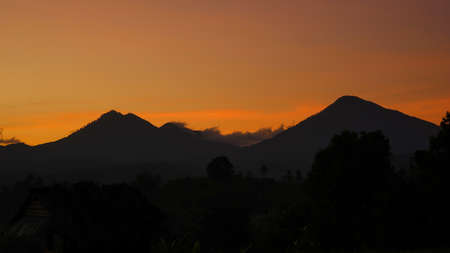 A view of the silhouette of mountains and trees at sunriseの写真素材