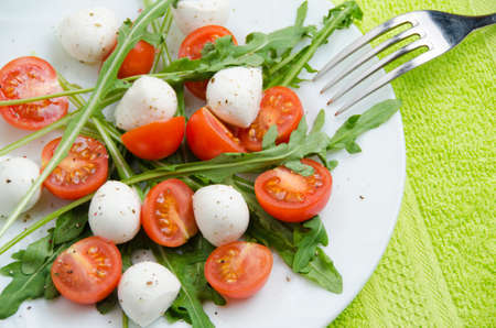 Fresh salad of arugula, cherry tomatoes and mozzarella on a white plate and a green napkin, top viewの写真素材