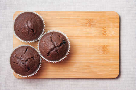 Three chocolate muffins on the wood cutting board on the  linen napkin with space for textの写真素材
