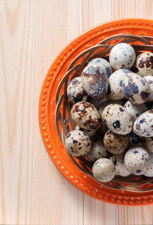 Quail eggs in wicker bowl and orange plate, standing on wooden boards, top view, cropの写真素材