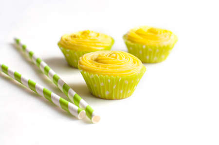 Cupcakes with yellow cheese cream in light green paper baking cups and striped drinking straws on white background. Selective focusの写真素材