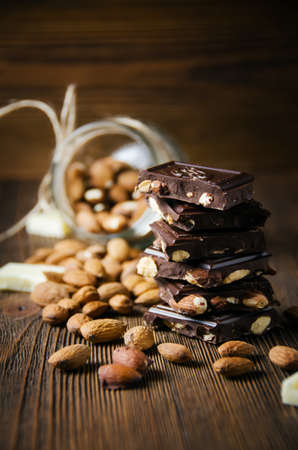 Broken dark chocolate with nuts and almonds on wooden background. Selective focus