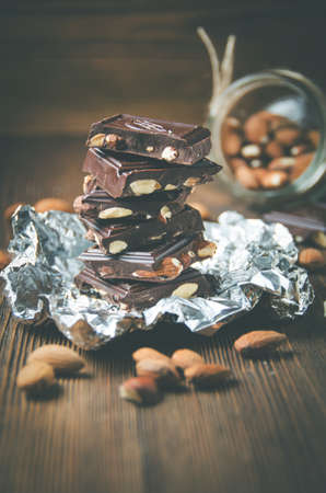 Broken chocolate bar on foil, sprinkled with cocoa powder and scattered almonds on wooden table. Low contrast, toned. Selective focusの写真素材