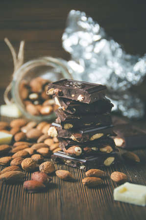 Broken dark chocolate with nuts and almonds on wooden background. Low contrast, toned. Selective focusの写真素材