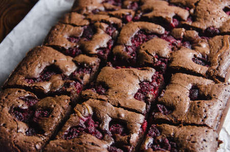 Brownie with raspberry on a baking paper and wooden countertop, close-up