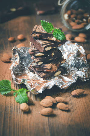 Dark chocolate with nuts, powdered with cocoa, mint leaves, almonds scattered on wooden table. Low contrast, toned. Selective focusの写真素材