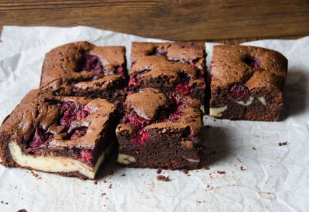 Raspberry brownie stuffed with cheesecake on baking paper on wooden backgroundの写真素材