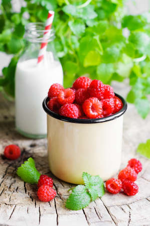 Fresh raspberries in cup, milk in glass bottle and mint on wooden rustic table
