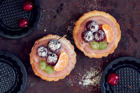 Fruit mini tarts with cherry on rusty background, flat lay