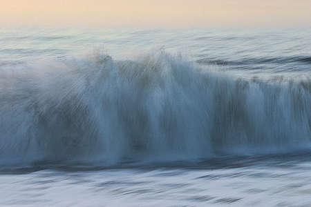 Feathery, crashing waves and blue ocean with soft orange skyの写真素材