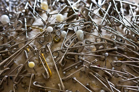 Macro shot of safety pins and pearl-tipped straight pins clustered in an old pin cushionの写真素材