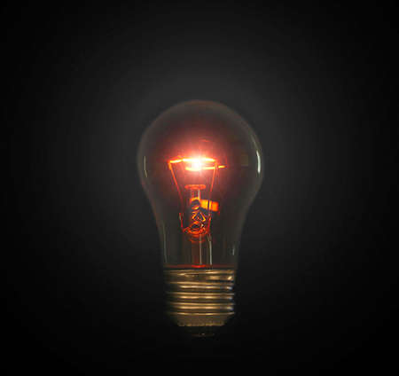 Macro photo of a glowing light bulb on a black background - showing all the intricacies of the glowing filament insideの写真素材