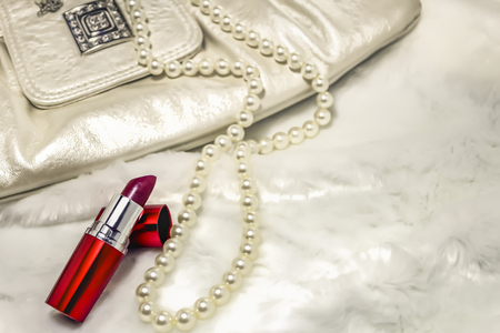 Women's clutch, lipstick, necklace on white furの写真素材