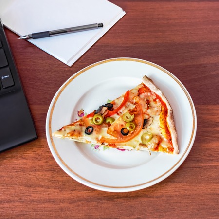 A piece of pizza on the desktop. Lunch break in the office. Flat lay.の写真素材