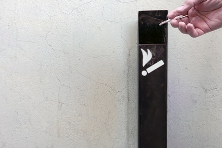 The man throws a cigarette butt in the ashtray on the wall in the street.