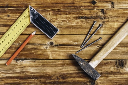 Nails, old hammer, pencil and measuring angle on wooden background