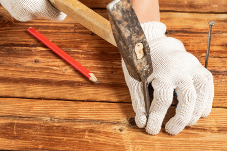 A man in white gloves is hammering a nail on wooden surfacesの写真素材