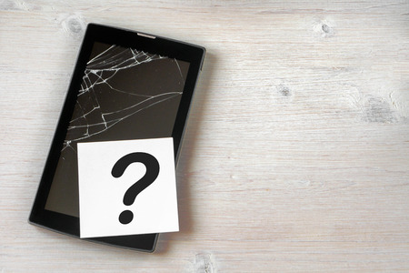 Broken tablet computer with cracked screen and a question mark on wooden background. Copy space